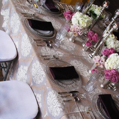 Elegant table display with custom linens, silver rimmed glass plates, candle sticks, pink and white roses